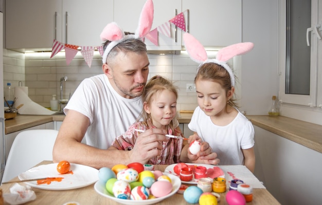 Un padre felice con due giovani figlie dipinge le uova di Pasqua e si prepara per le vacanze di Pasqua