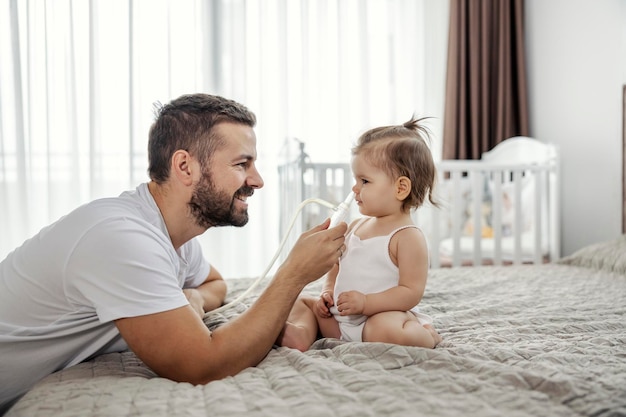 Un padre felice sta pulendo il naso del suo bambino con la pompa in una camera da letto