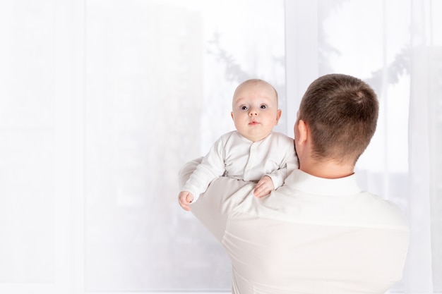 Un padre tiene un neonato sulla spalla a casa vicino alla finestra, il concetto di una famiglia felice e amorevole, la festa del papà