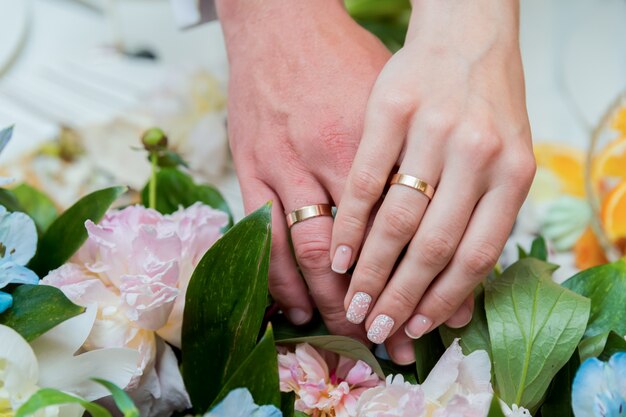 Un paio di fedi in oro sulle mani di una sposa e dello sposo. Avvicinamento.