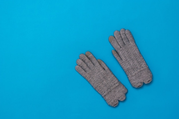 Un paio di guanti lavorati a maglia grigi per le donne su sfondo blu. Accessori da donna per il freddo.
