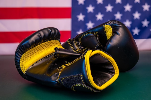 Un paio di guantoni da boxe neri e gialli su un tavolo verde con una bandiera americana sullo sfondo.