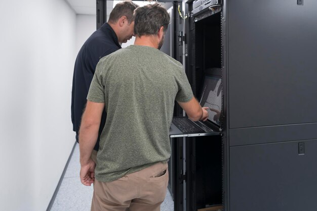 Un paio di ingegneri del server collaborano in data center ad alta tecnologia. Il team di tecnici aggiorna l'hardware ispezionando le prestazioni del sistema nella sala server dei super computer o nella farm di mining di criptovaluta.