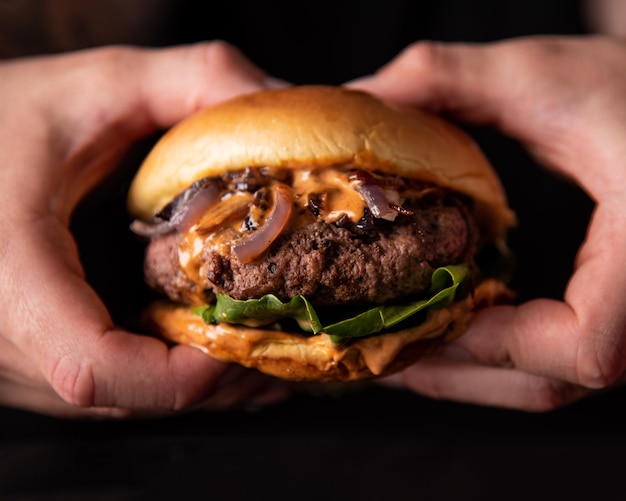 Un paio di mani che tengono un hamburger fresco e succoso con cipolle di lattuga e formaggio su sfondo nero