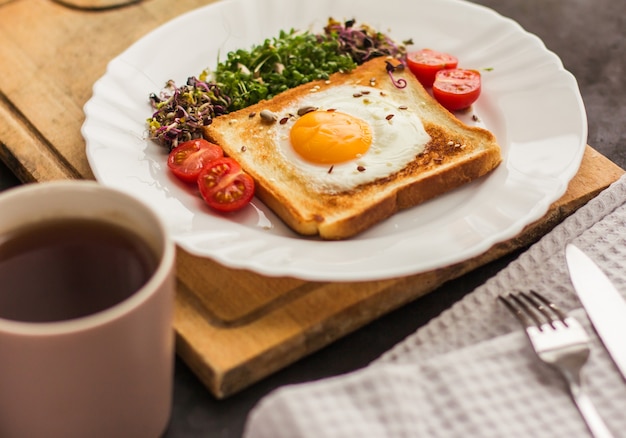 Un panino con l'uovo nel foro del pane, microgreens, cibo sano Colazione, una tazza di tè