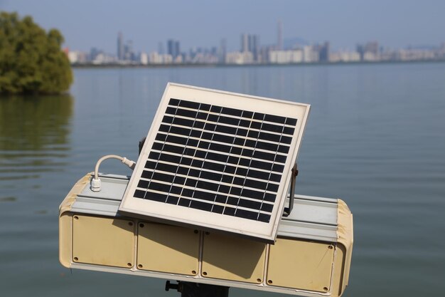 Un pannello solare montato sulla parte superiore di una scatola elettrica con lo skyline sullo sfondo sullo sfondo di acqua e vegetazione