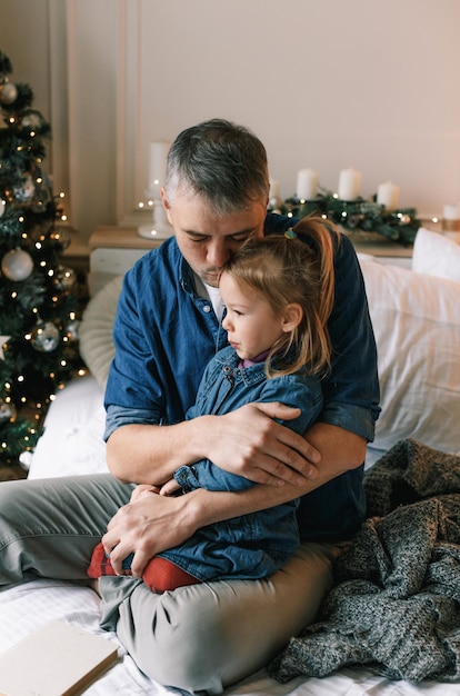 Un papà allegro bacia una figlia carina vicino all'albero di Natale