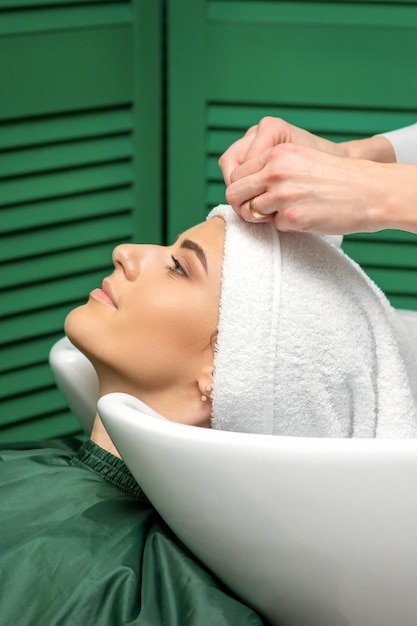 Un parrucchiere avvolge una testa femminile in un asciugamano dopo aver lavato i capelli nel salone di bellezza.