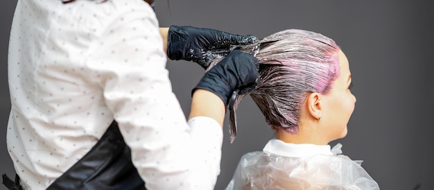 Un parrucchiere sta applicando il colore ai capelli di un cliente. Colorazione dei capelli in un salone di bellezza. Concetto di bellezza e persone. Vista posteriore ravvicinata.