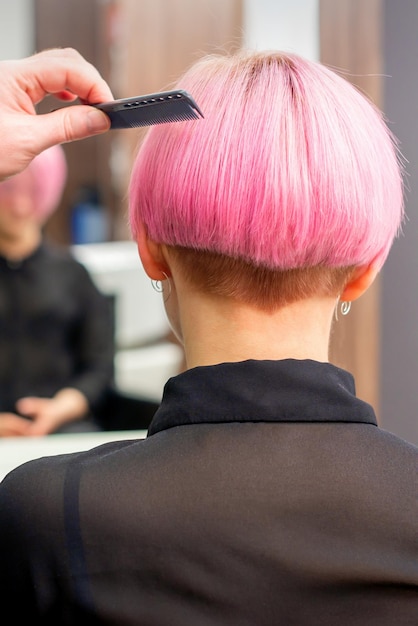 Un parrucchiere sta pettinando i capelli corti rosa tinti della cliente femminile nella vista posteriore del parrucchiere