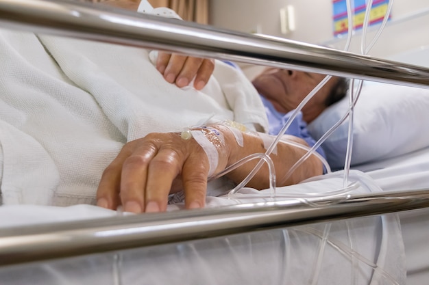 Un paziente in ospedale con soluzione fisiologica per via endovenosa, in mano di uomo anziano asiatico