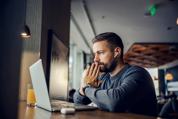 Un pensieroso imprenditore causale è seduto in un bar e guarda il laptop