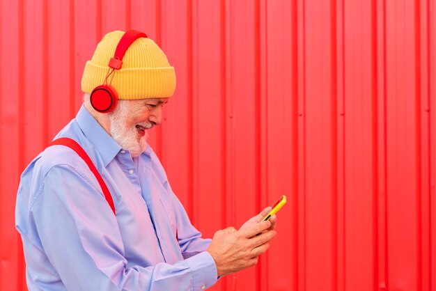 Un pensionato moderno che ascolta musica con le cuffie mentre invia messaggi sul cellulare