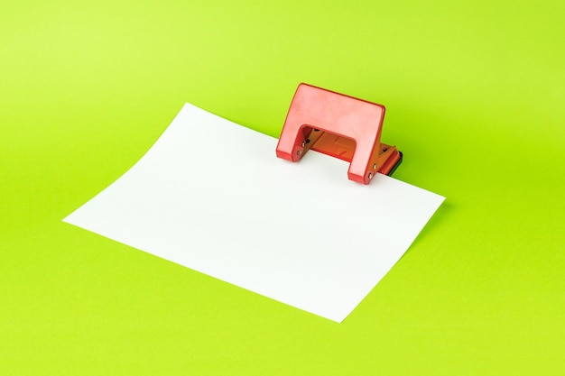 Un perforatore rosso con un foglio di carta bianco su sfondo verde