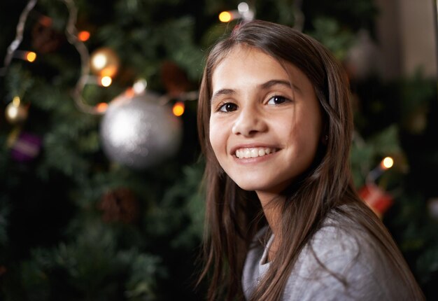 È un periodo gioioso dell'anno Scatto di una bambina seduta vicino a un albero di Natale