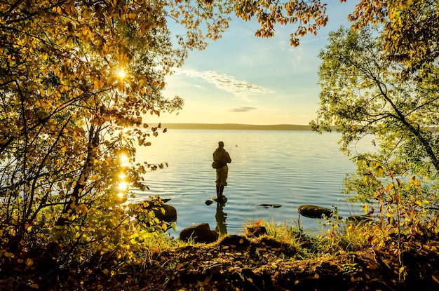 Un pescatore si erge su una roccia nel lago in una mattina d'autunno.