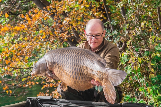 Un pescatore tiene in mano un'enorme carpa vicino al lago di Bled