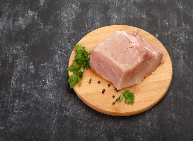 Un pezzo di carne cruda con erbe si trova su un tagliere di legno su sfondo nero.