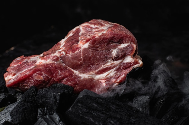 Un pezzo di carne di maiale cruda sul primo piano dei carboni