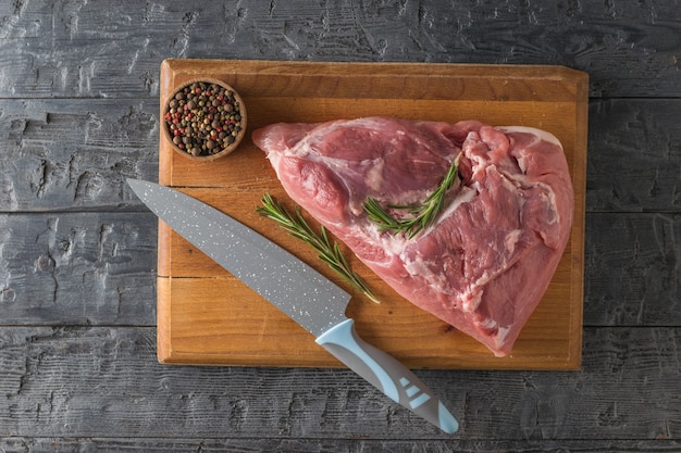 Un pezzo di carne di maiale su un tagliere con un coltello e condimenti. Ingredienti per la cottura di piatti di carne. La vista dall'alto.