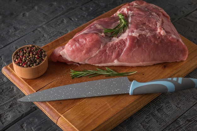 Un pezzo di carne di maiale su un tagliere con un coltello e condimenti. Ingredienti per la cottura di piatti di carne.