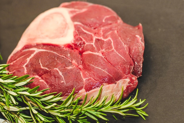 Un pezzo di carne fresca, una grande bistecca di manzo sull'osso ossobuco con un ramoscello di rosmarino su uno sfondo nero