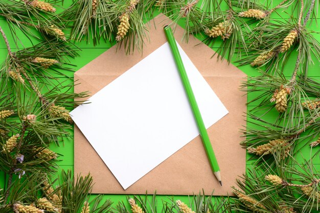 Un pezzo di carta bianco con una busta tra i rami di pino su uno sfondo di legno verde