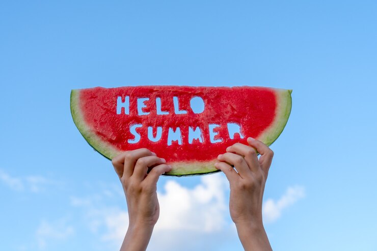 Un pezzo di cocomero contro un cielo blu. Le mani dei bambini tengono in mano una fetta di cocomero con il testo Hello Summer. Concetto di ora legale.