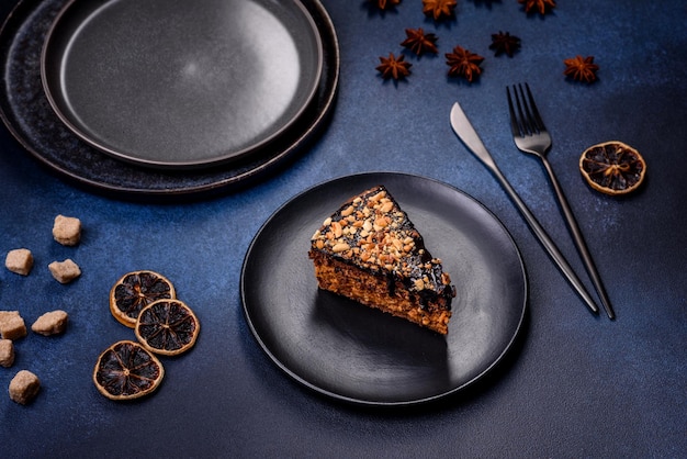 Un pezzo di deliziosa torta fresca con noci e cioccolato su un piatto nero su uno sfondo blu scuro