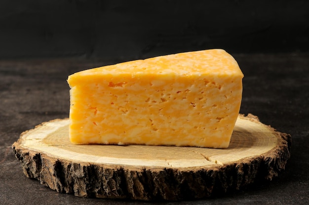 Un pezzo di delizioso formaggio marmorizzato su un supporto di legno su uno sfondo scuro. avvicinamento