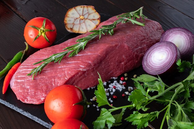 Un pezzo di filetto di manzo su un piatto di pietra nera con spezie e verdure fresche.