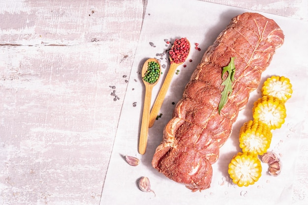 Un pezzo di lonza di maiale cruda. Carne fresca marinata legata con spago culinario, mais dolce e spezie. Una luce dura alla moda, un'ombra scura, un vecchio tavolo di legno, vista dall'alto