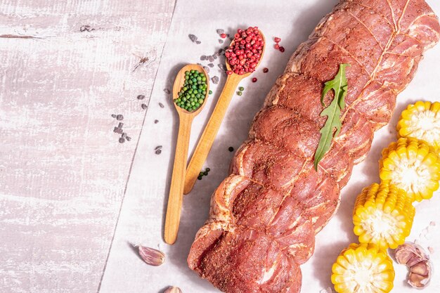 Un pezzo di lonza di maiale cruda. Carne fresca marinata legata con spago culinario, mais dolce e spezie. Una luce dura alla moda, un'ombra scura, un vecchio tavolo di legno, vista dall'alto