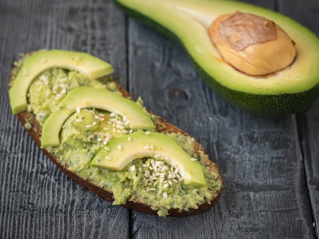 Un pezzo di pane spalmato di avocado con pezzi di frutta su un tavolo di legno.