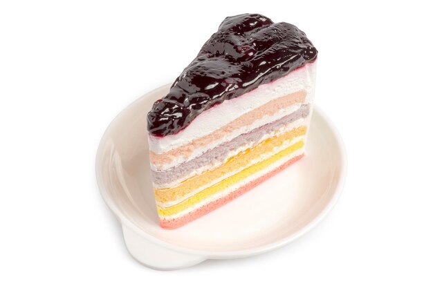 Un pezzo di torta arcobaleno con salsa di mirtilli servita in un piatto bianco isolato su bianco