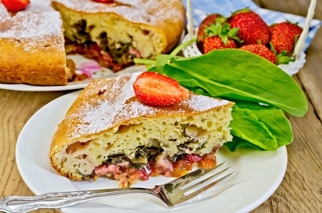 Un pezzo di torta dolce con fragole e acetosa, tovagliolo, torta, forchetta sullo sfondo di tavole di legno