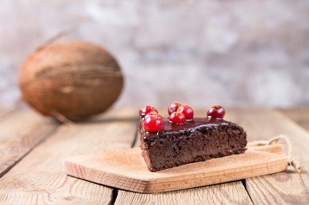 Un pezzo di torta senza glutine al cioccolato, decorata con mirtilli rossi, su uno sfondo sfocato. In fondo è una noce di cocco.