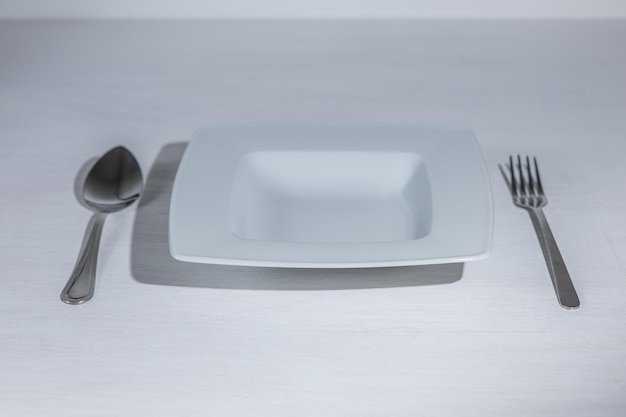 Un piatto bianco vuoto con cucchiaio e forchetta. Sfondo chiaro