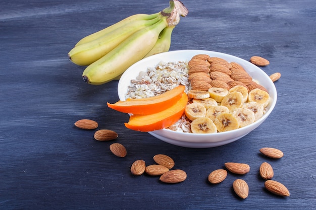 Un piatto con muesli, mandorle, banana, cachi su un fondo di legno nero con lo spazio della copia.