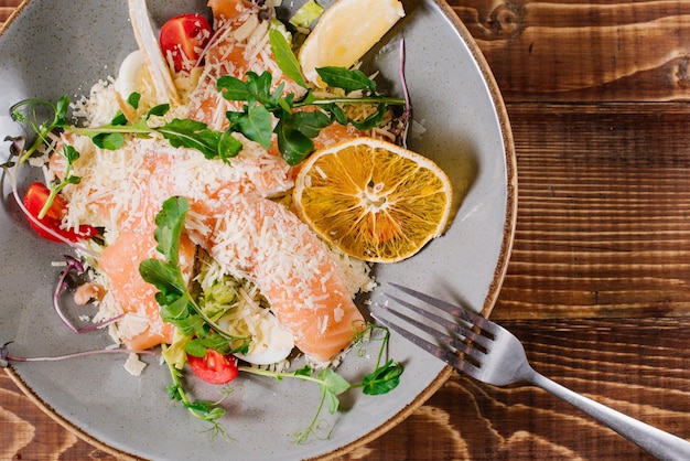 Un piatto con salmone, verdure ed erbe aromatiche su fondo di legno