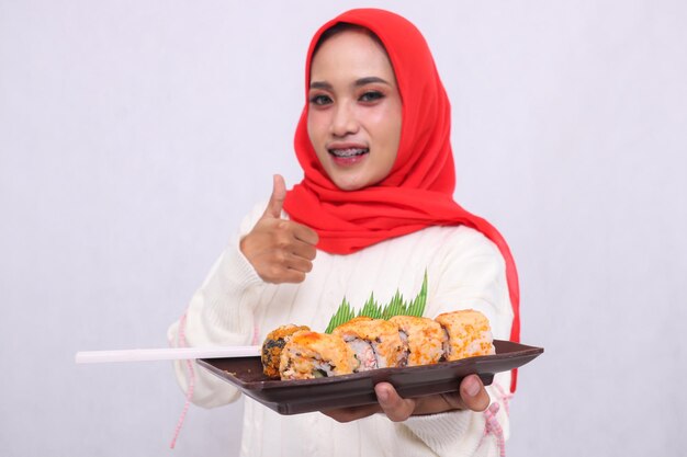un piatto contenente sushi cibo giapponese tenuto da una bella donna asiatica mentre sorride con un pollice