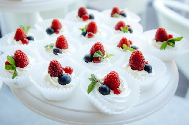 Un piatto da dessert bianco con sopra una tazza di panna montata e frutti di bosco.