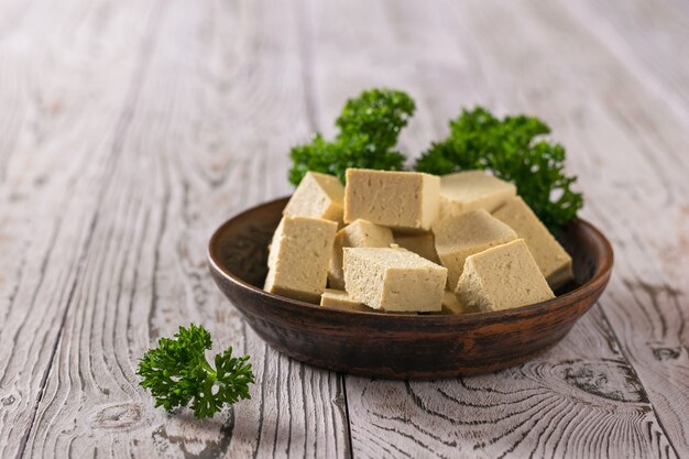 Un piatto di argilla con tofu e foglie di prezzemolo riccio su un tavolo di legno. Prodotto vegetariano.