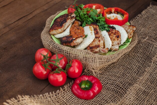 Un piatto di carne cotta, formaggio e verdure su un tavolo di legno. Vicino al tessuto della tela da imballaggio della tovaglia della tessile