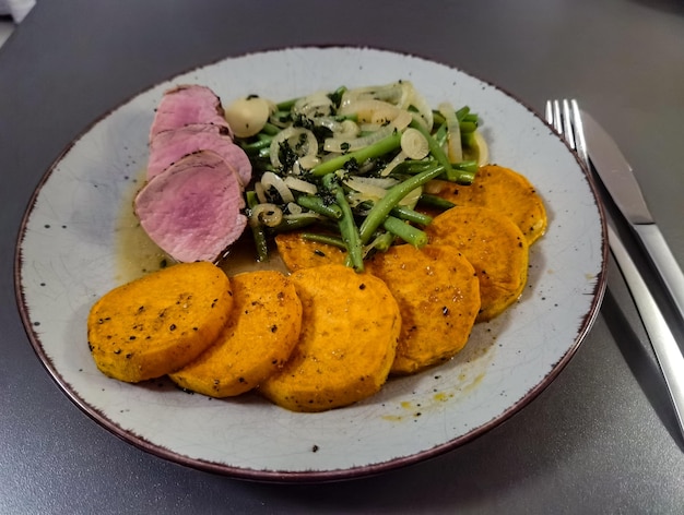 Un piatto di cibo con patate dolci a fette e fagiolini.