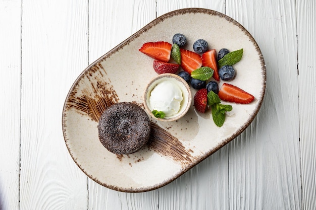 Un piatto di cupcake al cioccolato con fragole e mirtilli su un tavolo di legno bianco.