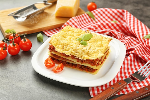 Un piatto di gustose lasagne su una tavola grigia.