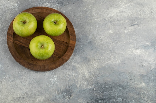 Un piatto di legno di tre mele verdi fresche sulla superficie di marmo.