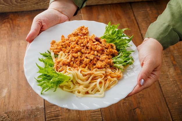 Un piatto di pasta al ragù alla bolognese in mani femminili. Foto orizzontale