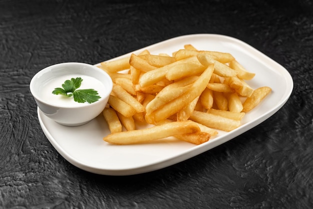 Un piatto di patatine fritte con una salsa bianca sul lato